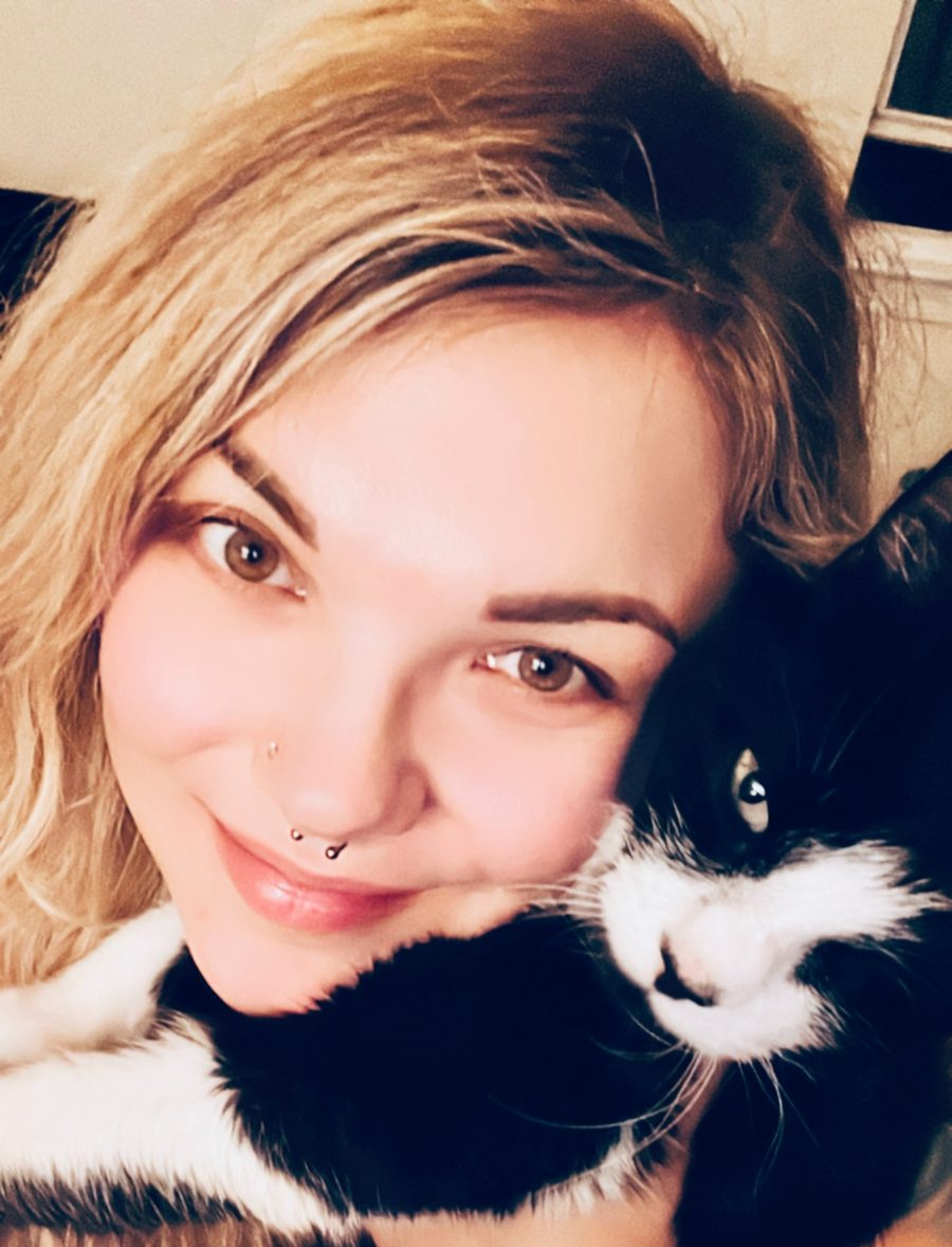 Jordana, owner of Comfy Claws, smiling while holding Eli, her one-eyed tuxedo cat